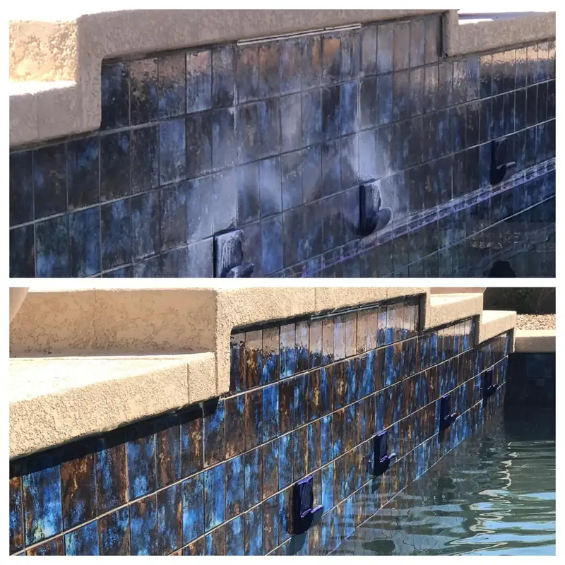 A spillway wall of dark iridescent glass tile with three scuppers, clouded white with calcium above and glossy blue and gold below
